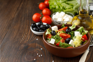 Tasty greek salad with feta, olives and tomatoes in a bowl on wooden background.