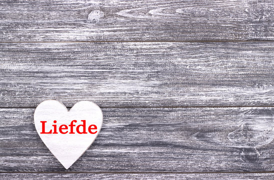 Decorative white wooden heart on grey wooden background with lettering Love in Dutch.