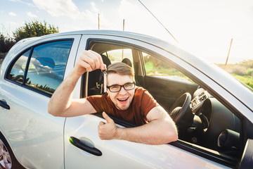 Naklejka premium Attractive young happy man showing his new car keys and laughing