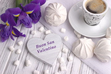 Still life with cup of coffe marshmallow zephyr iris flowers heart sign with lettering Happy Valentines Day in Italian on white wooden background.