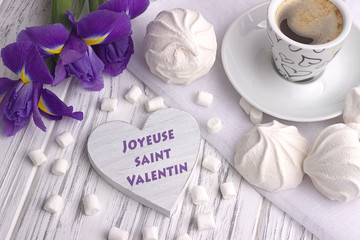 Still life with cup of coffe marshmallow zephyr iris flowers heart sign with lettering Happy Valentines Day in French on white wooden background.