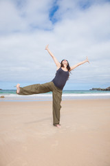 Obraz premium brunette brown hair pregnant woman with grey shirt green trousers and black sunglasses happy dancing in summer on sand beach ocean in Asturias Spain 