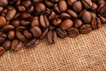 Naklejka premium coffee beans on burlap background. roasted coffee beans isolated in white background. Roasted coffee beans background close up. Coffee beans pile from top on white background with copy space for text
