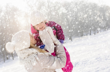 Mother having fun with daughter on winter day while falling snow