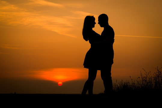 silhouette teenager lovers couple with sun between on sunset dusk sky background: black shadow hand drawn of people hug and kiss people:passion in love concept:decoration,design,valentines