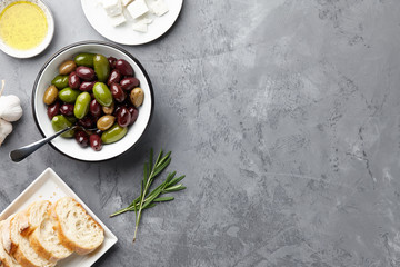 Fresh olives, feta cheese, rosemary, olive oil and ciabatta bread on gray stone background