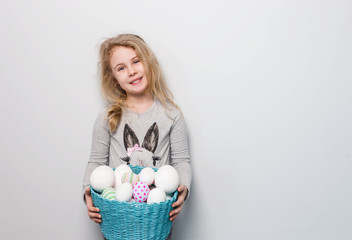 Little blonde girl holding basket with painted eggs. Easter day.