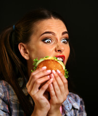 Woman eating hamburger. Girl wants to eat burger. Student consume fast food. Portrait of person with good appetite have greedily dinner delicious sandwich on a black background.