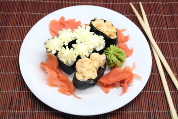 Sushi pieces on white plate and two chopsticks over brown wicker straw mat top view closeup