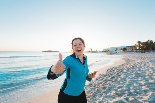 Smiling female runner show thumbs up. Summer day on the beach
