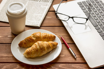 Business lunch with croissant and laptop on wooden desk
