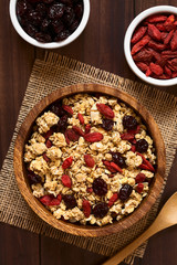Crunchy oatmeal cereal with almond, dried goji berries and cranberries, photographed overhead with natural light (Selective Focus, Focus on the top of the cereal and the berries)