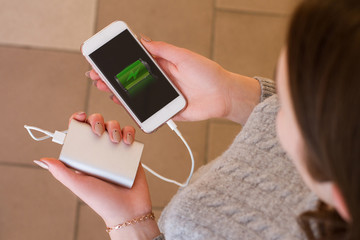 Girl hold in hands smart phone and power bank. Charge smart phone from power bank. Use modern gadget.