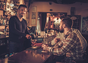 Cheerful old friends drinking draft beer at bar counter in pub.