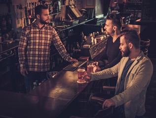 Cheerful old friends drinking draft beer at bar counter in pub.