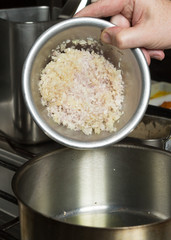 Minced garlic and finely sliced onion being dropped into a metal frying pan of olive oil. Step by step recipe cooking.