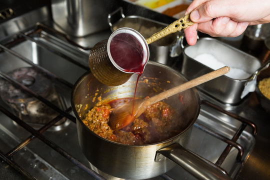 Sweet blended pomegranate sauce being poured into a hot frying pan of ingredients
