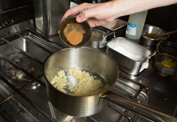 Turmeric powder being dropped into a pan of frying  minced garlic and finely sliced onion. Step by step recipe cooking.