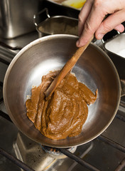 Rich thick brown curry paste being mixed and cooked in a metal frying pan, over a metal kitchen hob.
