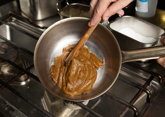 Rich thick brown curry paste being mixed and cooked in a metal frying pan, over a metal kitchen hob.