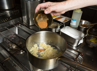 Turmeric powder being dropped into a pan of frying  minced garlic and finely sliced onion. Step by step recipe cooking.