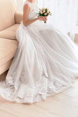 Fototapeta na wymiar Bride in beautiful dress with wedding bouquet sitting on sofa