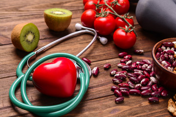 Red heart with stethoscope and healthy food on wooden background