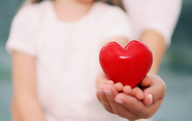 Hands of child and adult woman holding red heart, closeup