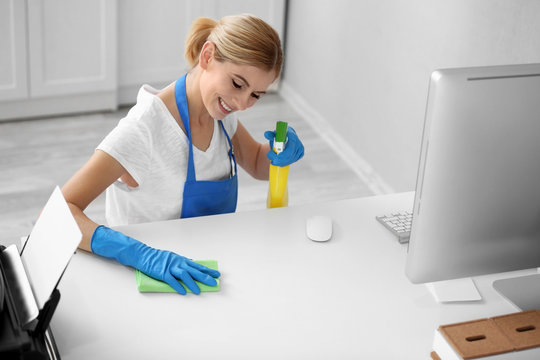 Pretty adult woman wiping table in office