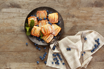 Sweet tasty pastries with bilberries on plate against wooden background, top view