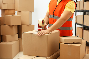 Closeup of man packing parcels with sticky tape at warehouse