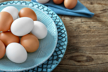 Plate with raw eggs on wooden background