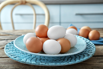 Plate with raw eggs on wooden table