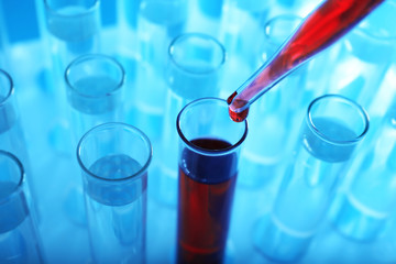 Closeup of a pipette dropping red sample into a test tube on blue background