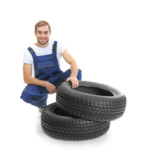 Young mechanic in uniform with tires on white background