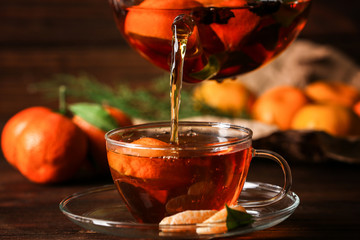 Pouring tangerine tea into cup on wooden background