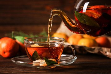 Pouring tangerine tea into cup on wooden background
