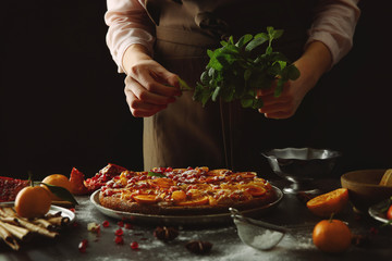 Woman chef decorating delicious tangerine pie on grey table