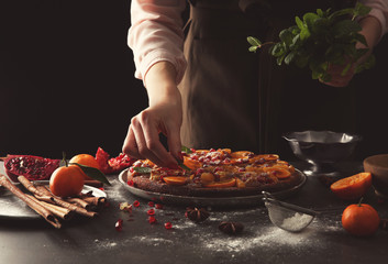 Woman chef decorating delicious tangerine pie on grey table