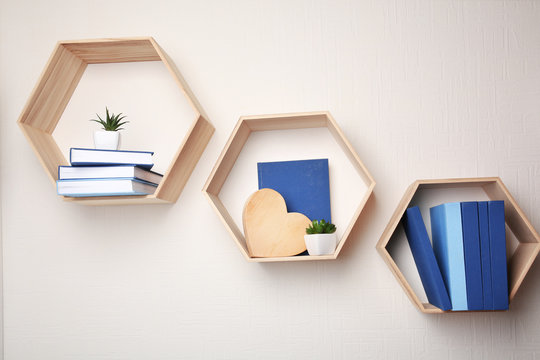 Different books on wooden shelves against light wall