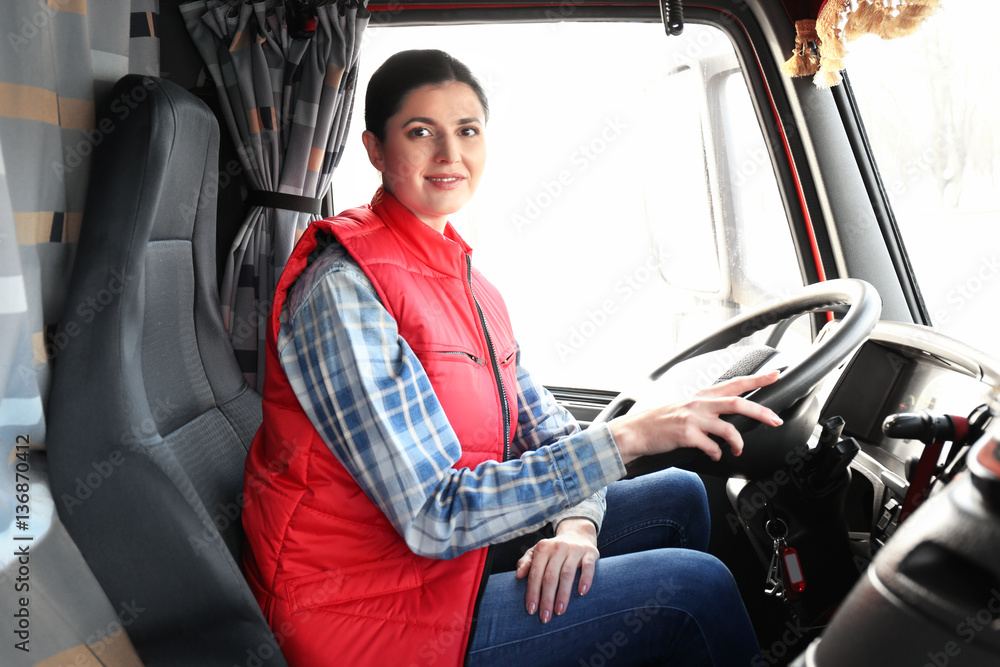 Wall mural young female driver sitting in cabin of big modern truck