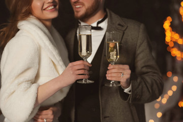 Happy wedding couple with glasses of champagne on winter evening, closeup