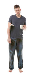 Young sleepy man in pajamas holding cup and newspaper on white background