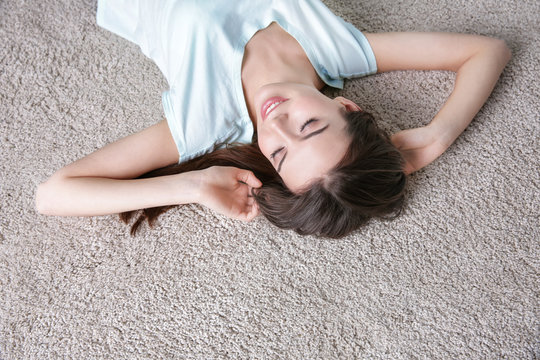 Happy young woman lying on soft floor in light room