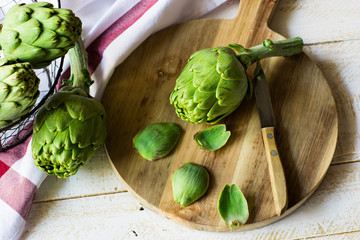 Peeled fresh artichoke preparing for cooking, wood cutting board, knife, vegetables in metal...