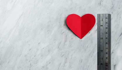 Red heart with ruler on white marble background.