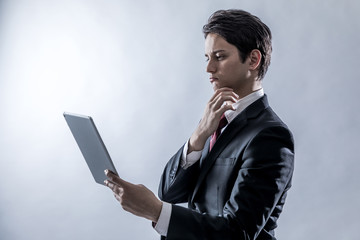 young businessman holding tablet PC and thinking something on white background