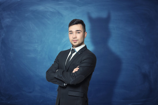 Businessman on blue chalkboard background with his shadow having devil horns.