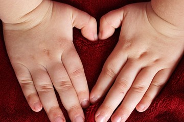 Hands of small girl making heart shape on red blanket