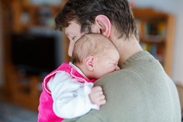 Happy proud young father holding his sleeping newborn baby daughter